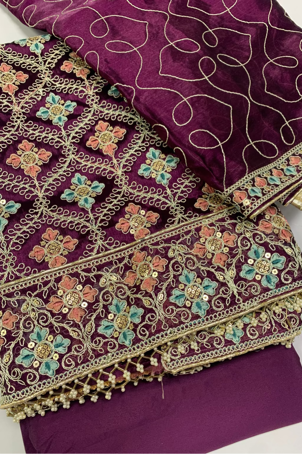 Purple fabric with intricate gold and multicolor embroidery on a white background