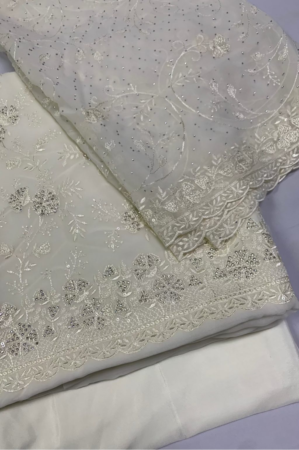 White fabric with intricate silver embroidery on a light purple background