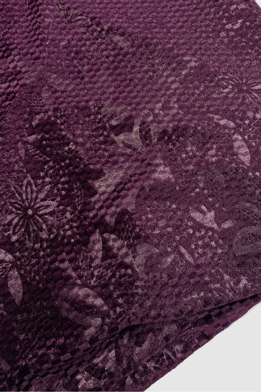 Close-up of a textured purple fabric with floral patterns on a white background