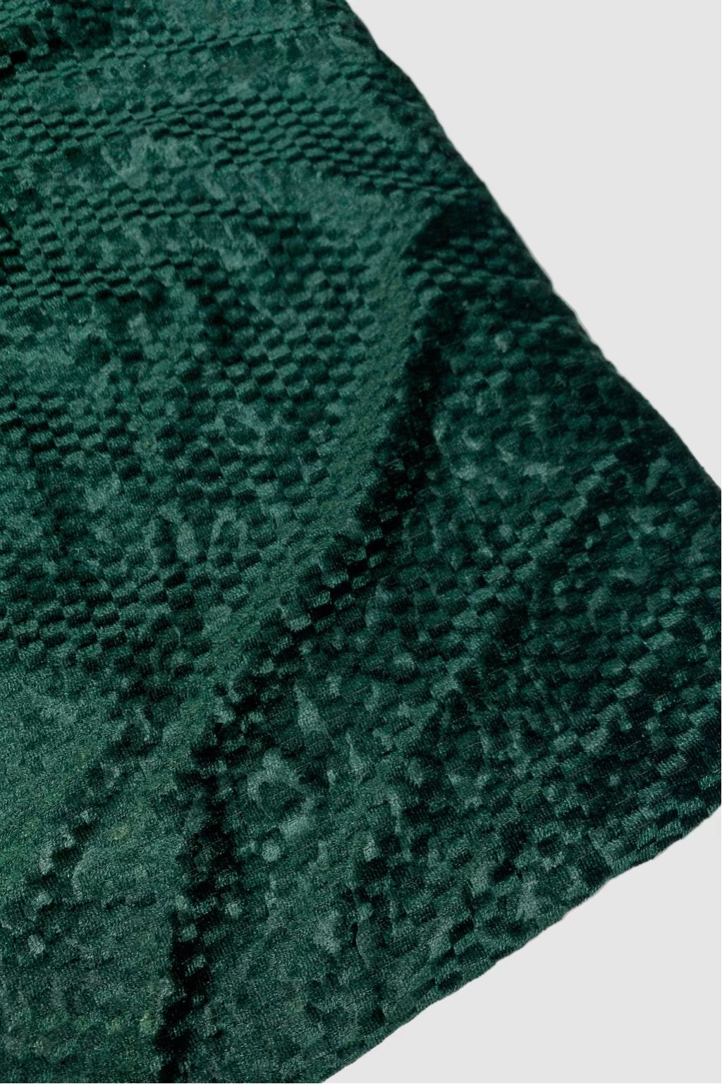 Close-up of a textured green fabric with a subtle pattern on a white background