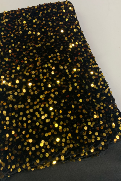 Black fabric with gold sequins on a plain background