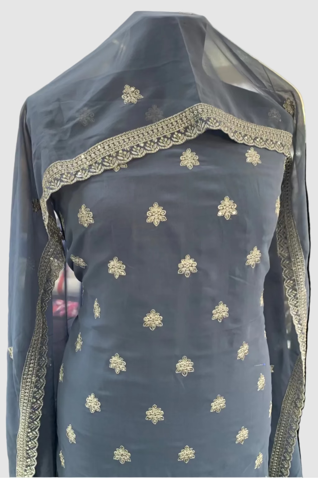 Grey embroidered garment with a sheer overlay in a store setting