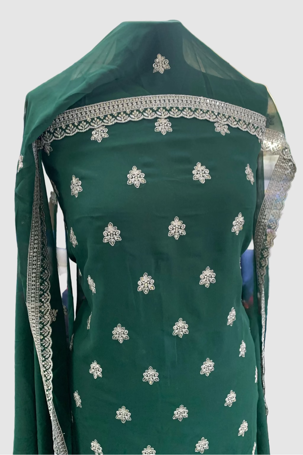Green embroidered garment with silver details on a mannequin in a store setting.