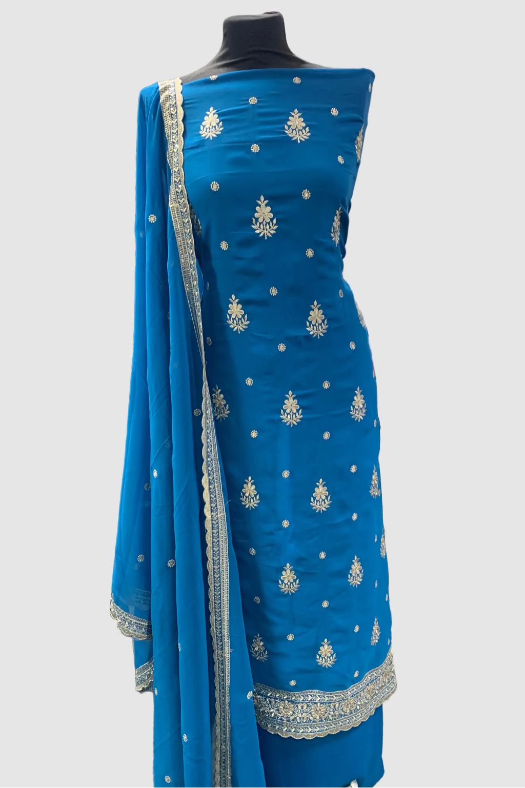Blue embroidered dress fabric with silver patterns on a mannequin in a store setting.