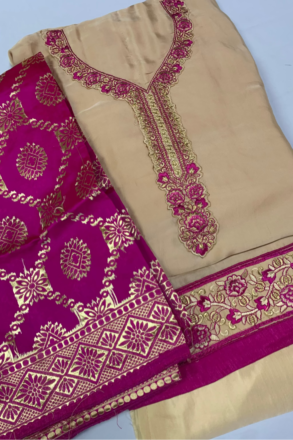 Beige fabric with intricate magenta and gold embroidery on a white background