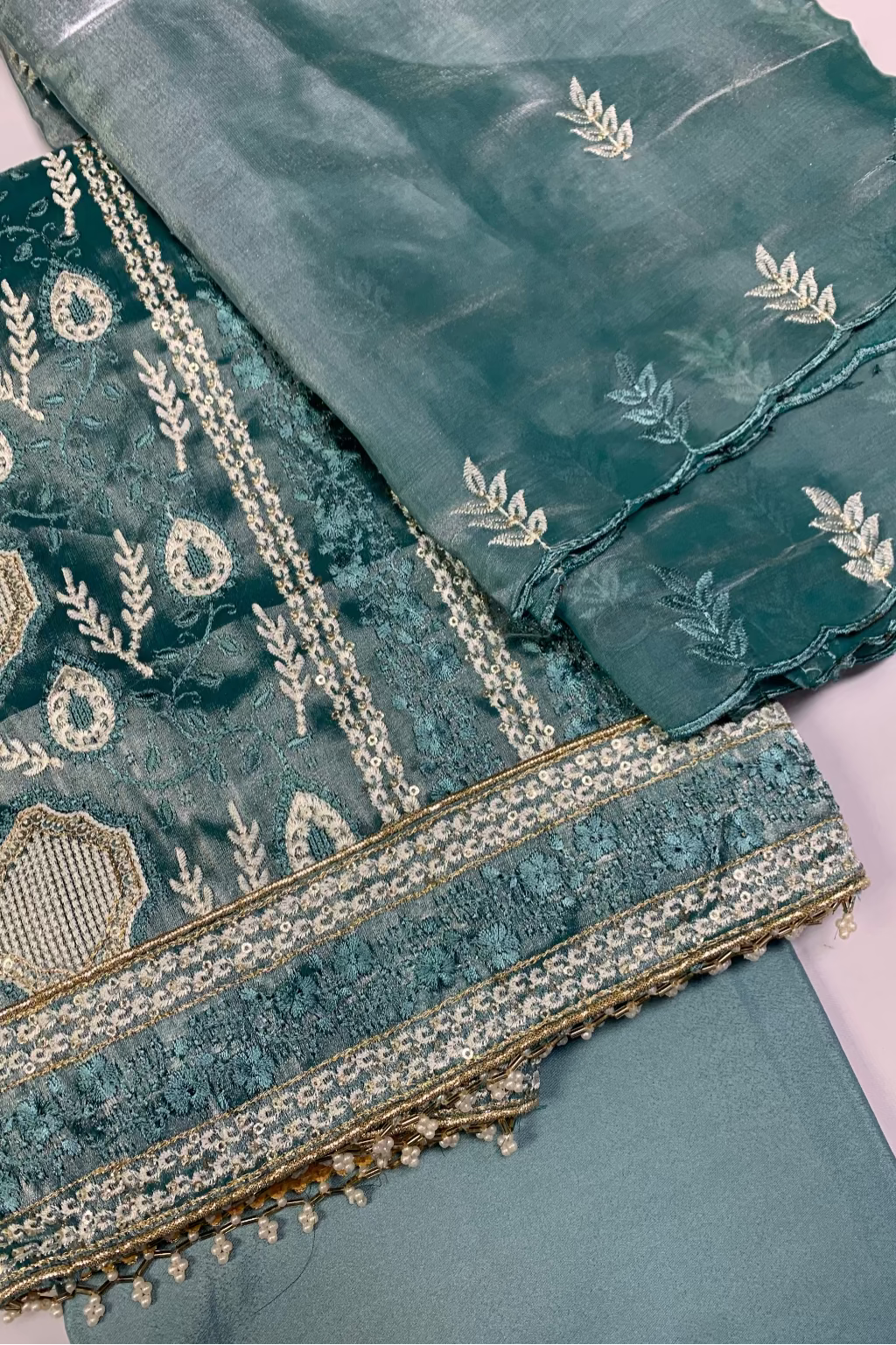 Teal fabric with intricate gold embroidery on a light background