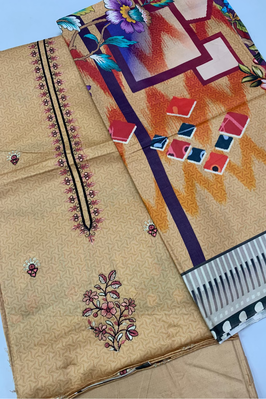 Beige fabric with floral embroidery and a colorful patterned fabric on a light blue background