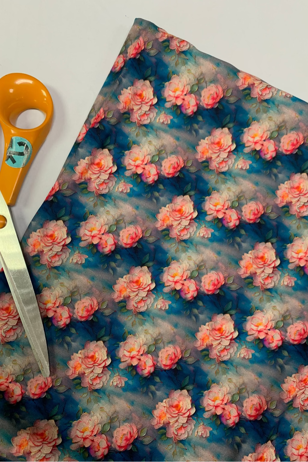 Floral-patterned fabric with pink flowers on a white background, accompanied by a pair of scissors.