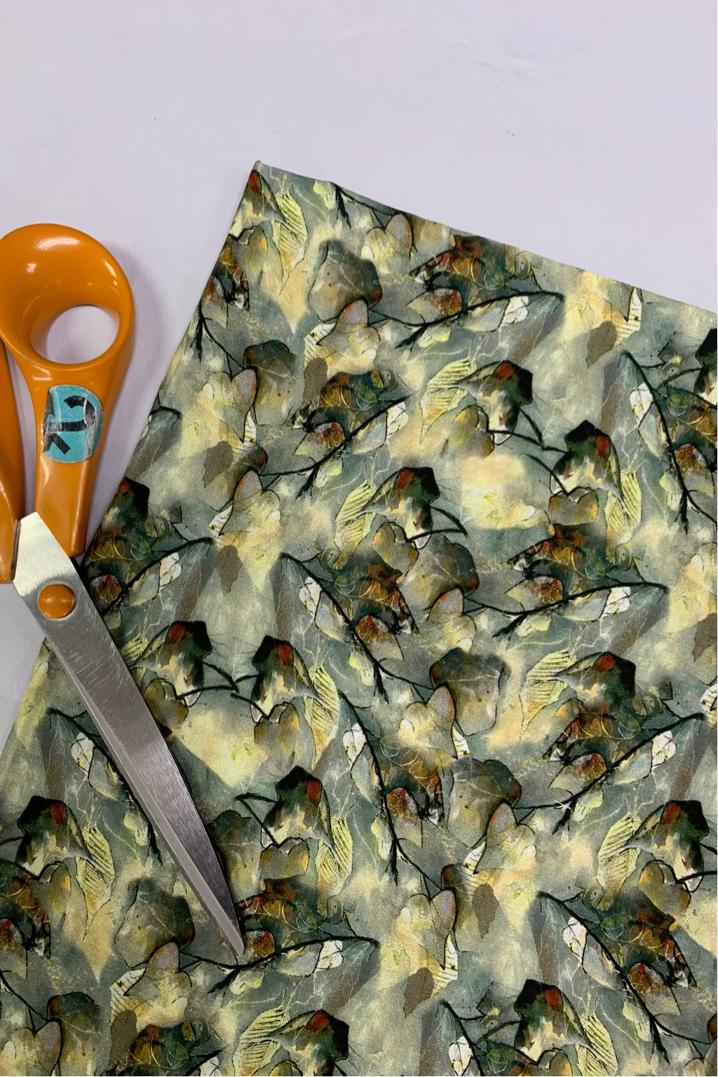 Piece of viscose fabric with a leaf design and a pair of scissors on a light purple background