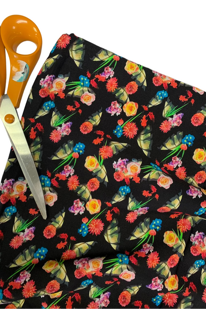 Floral-patterned fabric with colorful flowers on a black background, accompanied by orange-handled scissors.