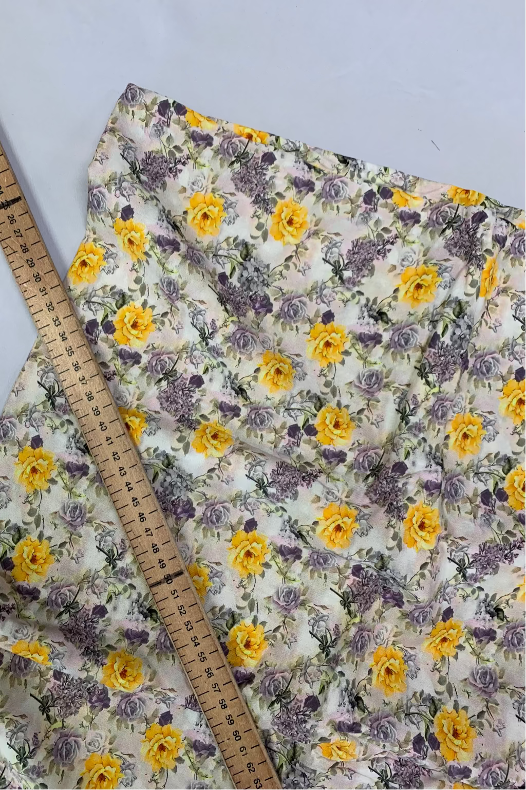 Floral fabric with yellow and purple flowers on a white background, accompanied by a wooden ruler for scale.