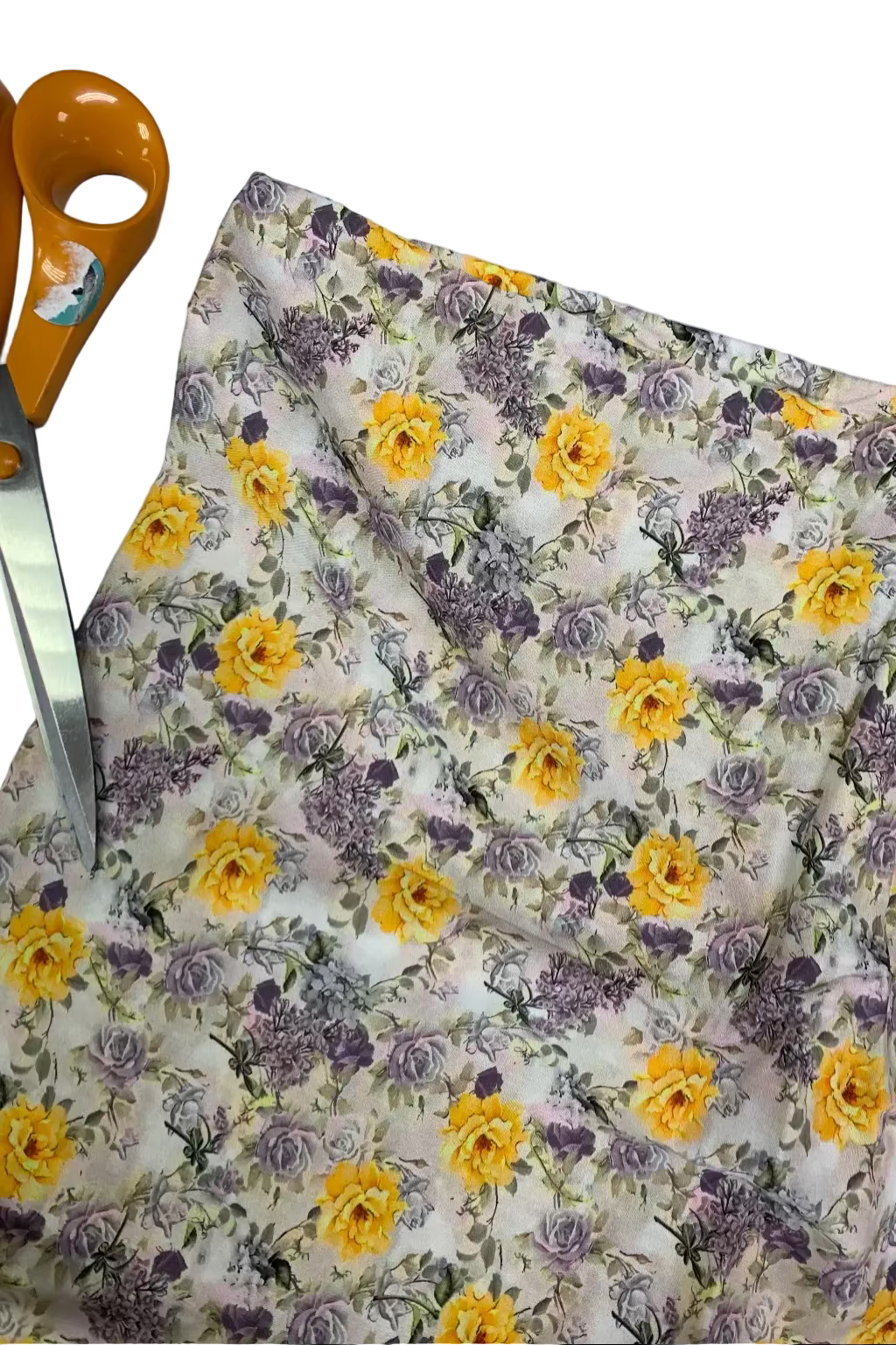Floral fabric with yellow and purple flowers on a white background, accompanied by orange-handled scissors.