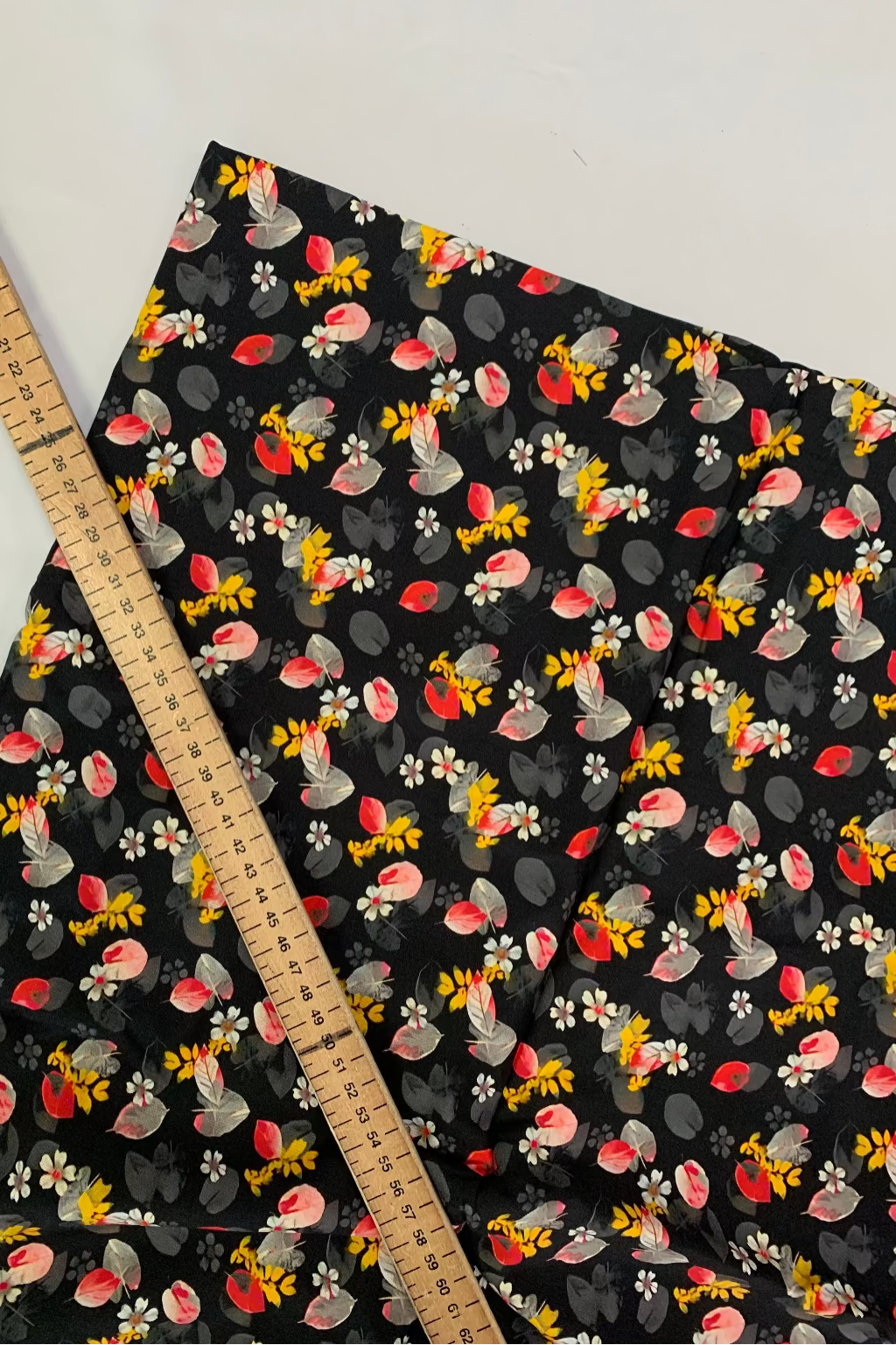 Fabric with colorful floral pattern on a black background, measured by a wooden ruler.