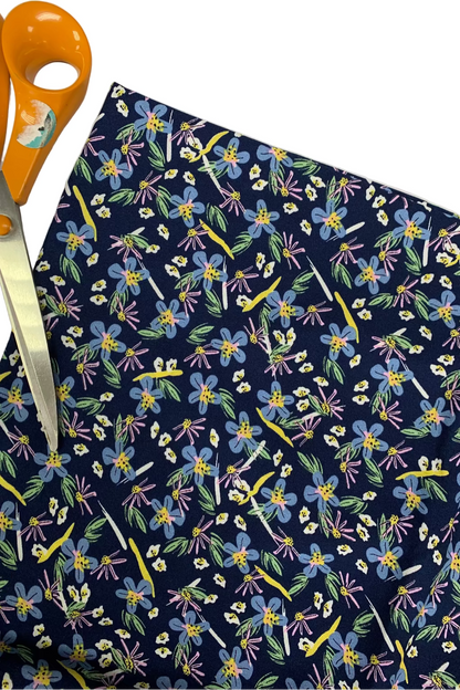 Floral-patterned fabric with colorful flowers on a navy background, accompanied by orange scissors.