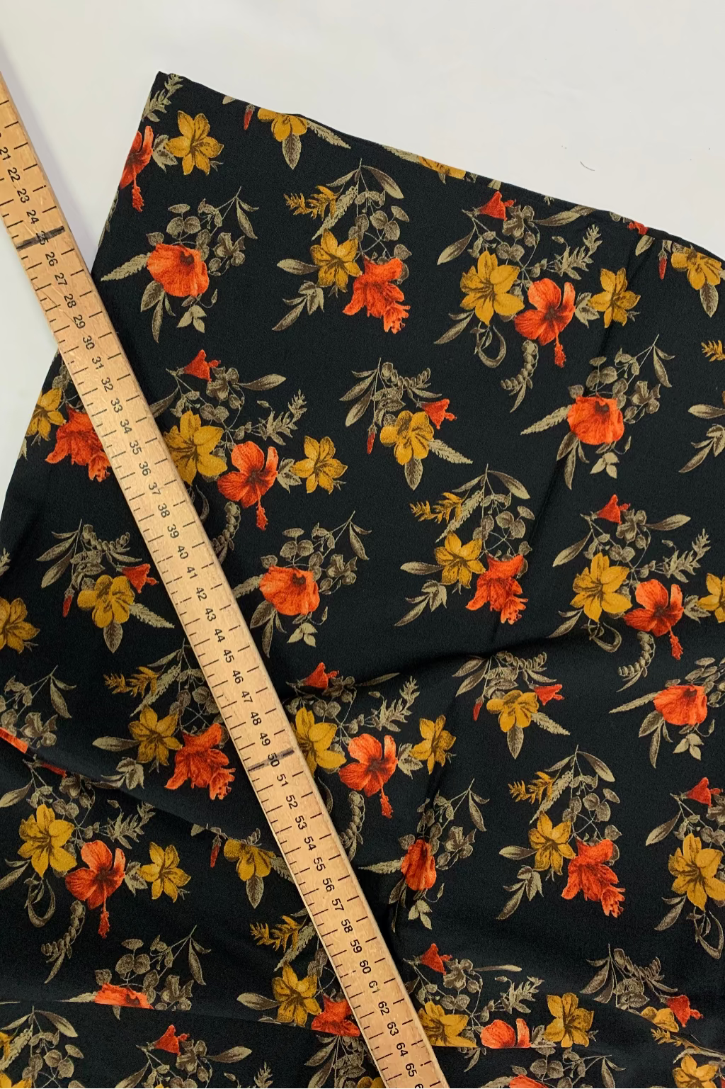 Floral fabric with orange and yellow flowers on a black background, accompanied by a ruler for scale.
