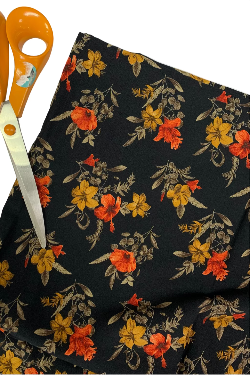 Floral fabric with orange, yellow, and red flowers on a black background, accompanied by orange scissors.