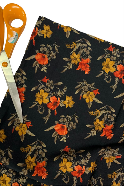 Floral fabric with orange, yellow, and red flowers on a black background, accompanied by orange scissors.