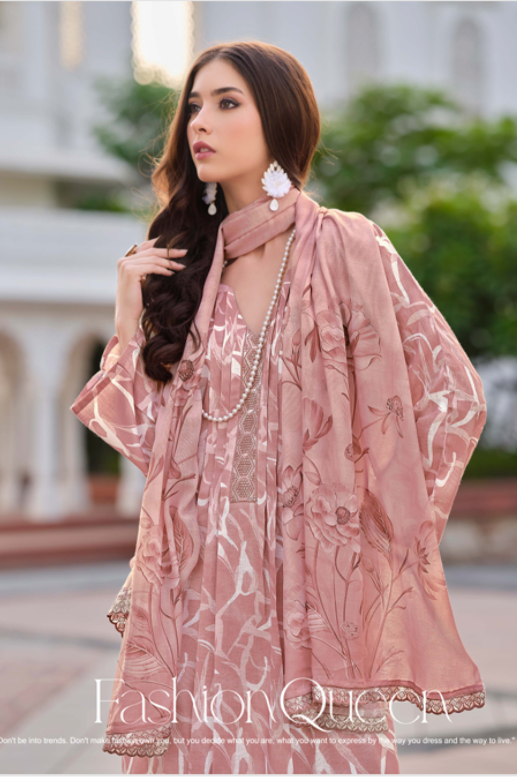 Woman modeling a pink traditional outfit with a white building in the background.