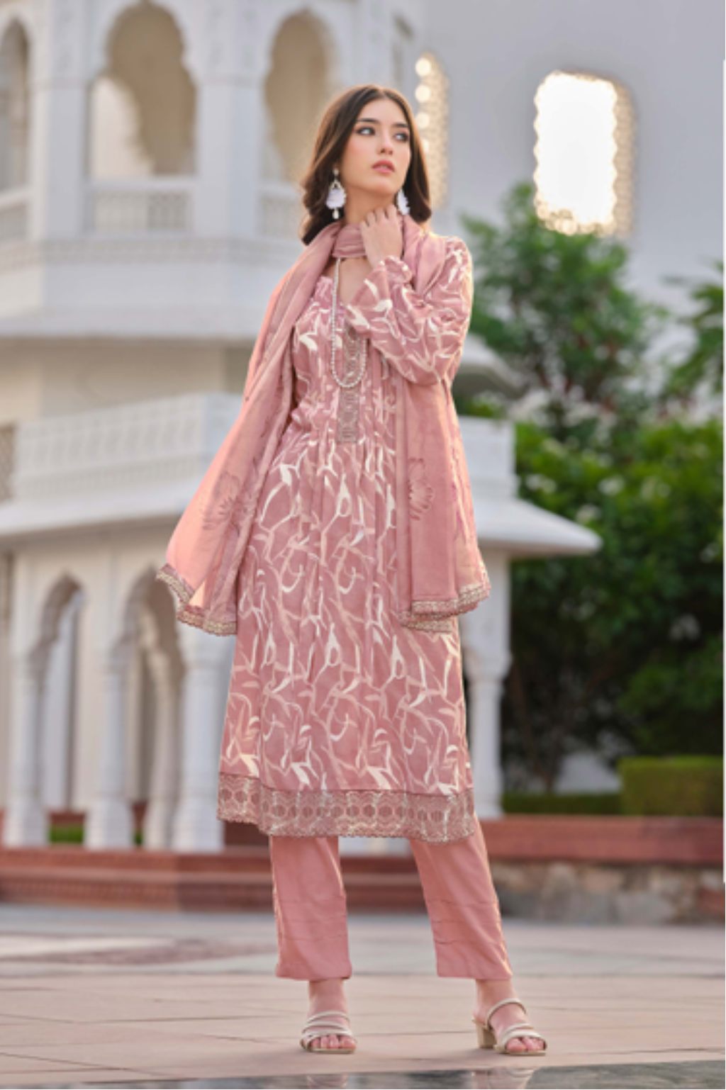 Woman modeling a pink traditional outfit with a white building in the background.