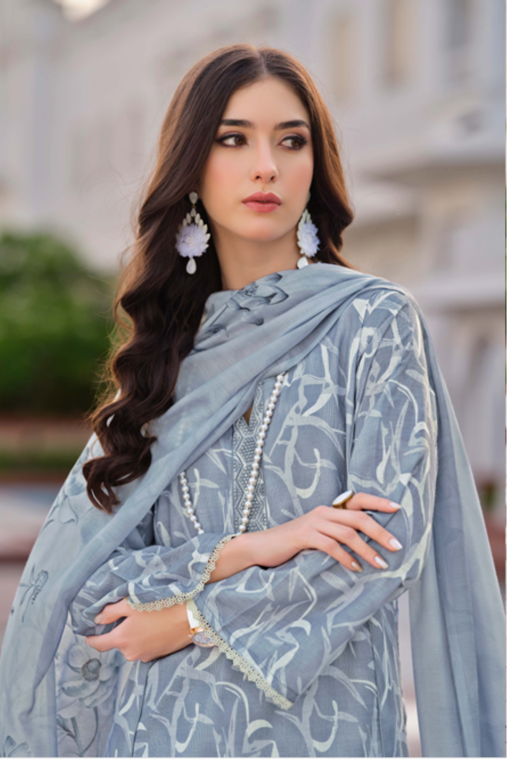 Woman wearing a light blue embroidered outfit in front of a building.