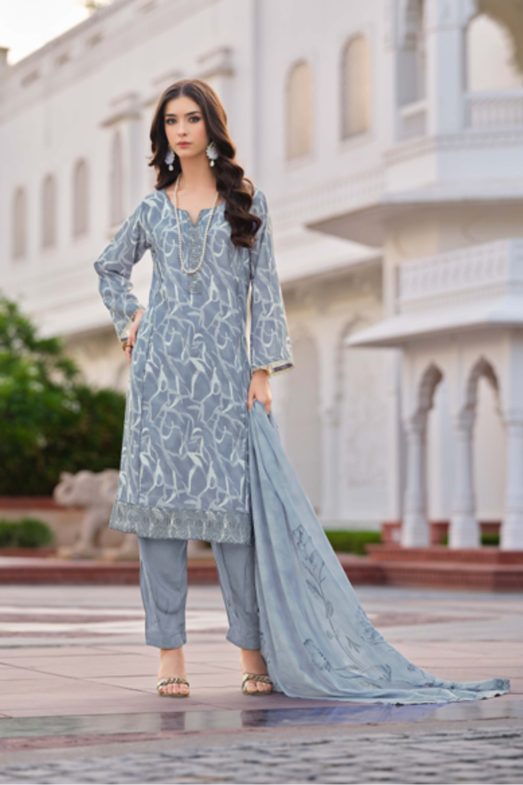 Woman wearing a light blue embroidered outfit in front of a building.