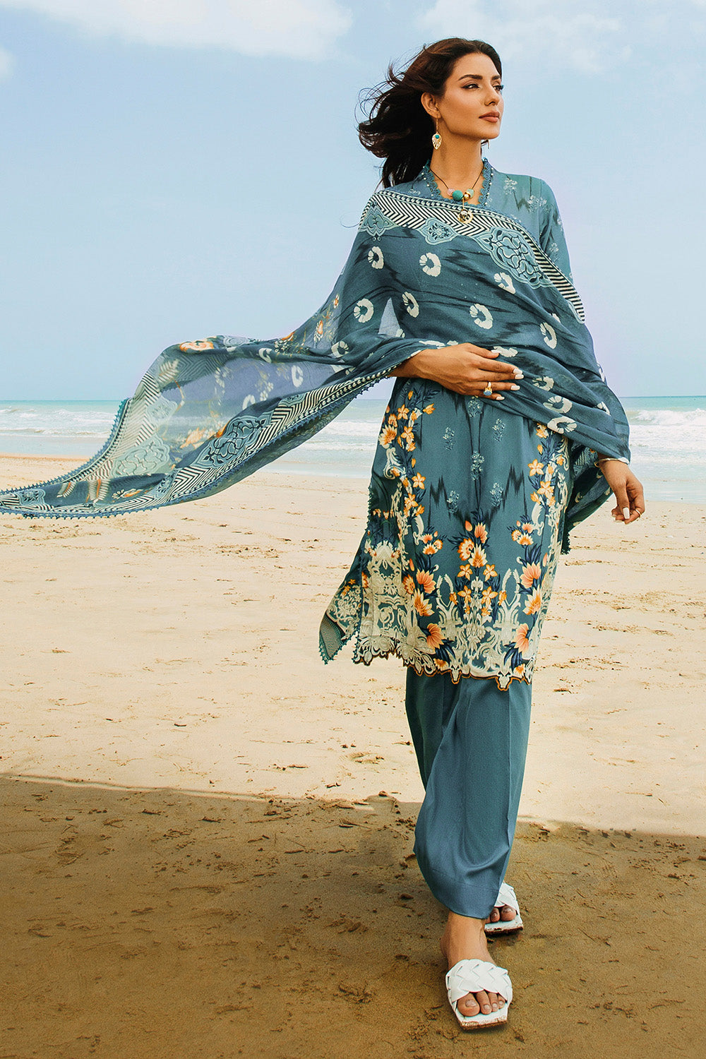 A woman wearing a traditional blue salwar kameez suit with digital printed floral patterns, consisting of a dupatta, shirt, and trousers.