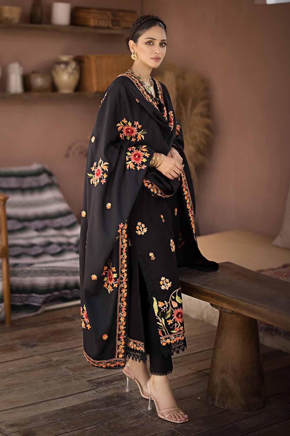 A woman wearing a black traditional salwar kameez suit with embroidered floral designs, featuring a dupatta, shirt, and dye-printed trouser.